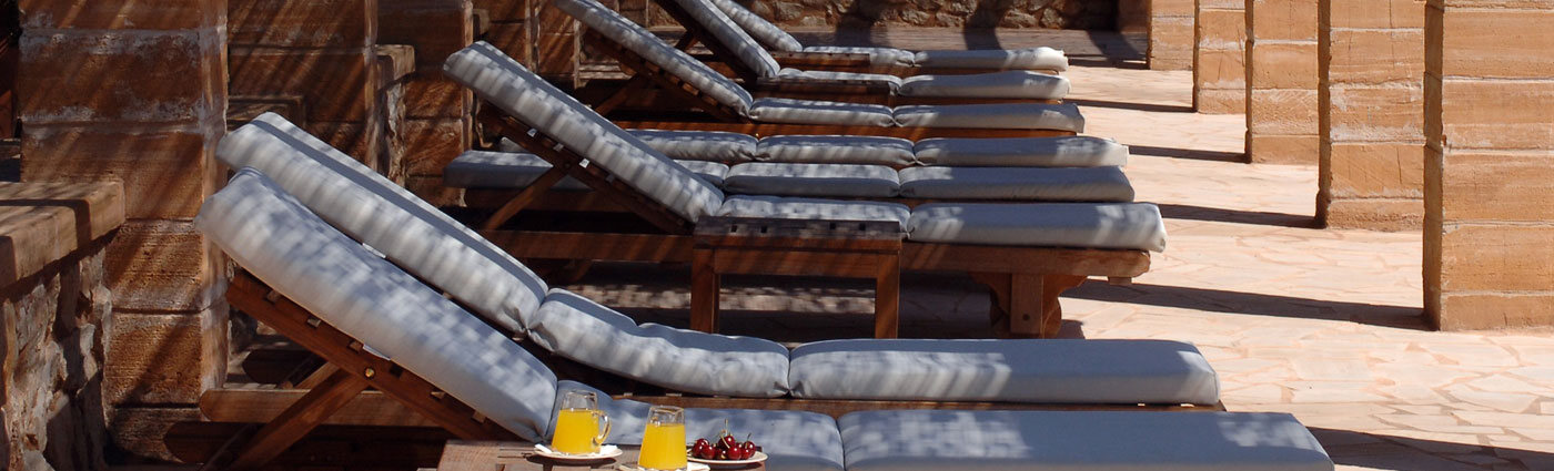 A row of cushioned sun-loungers on the marès terrace at Son Terrassa, with fresh orange juice and cherries in the morning light