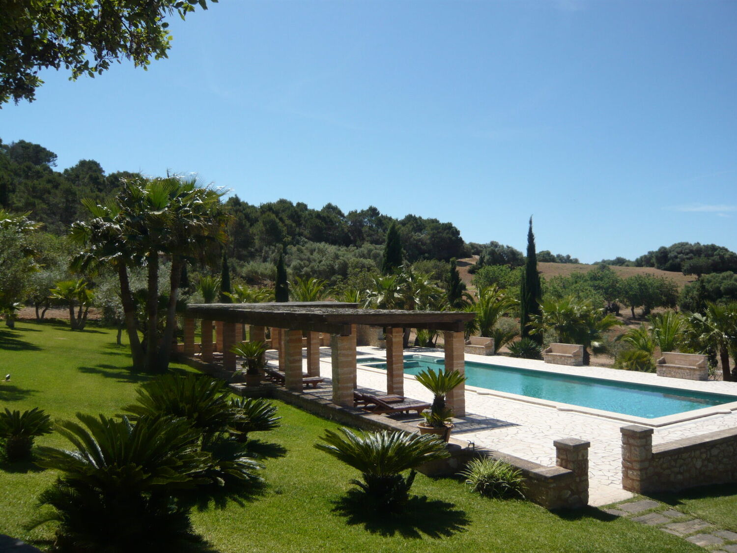 The Son Terrassa pool by day with a stone pergola, cypress trees and ancient olives, the hills of central Mallorca rising behind