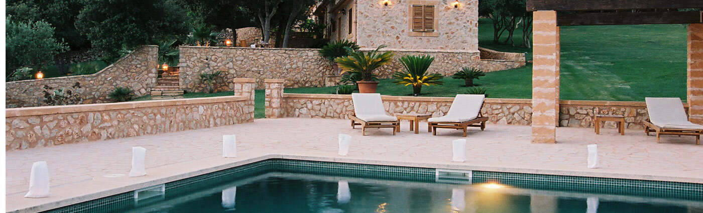 The Son Terrassa pool at dusk, the marès stone house and olive grove behind it, sun-loungers and candle-lanterns on the stone deck