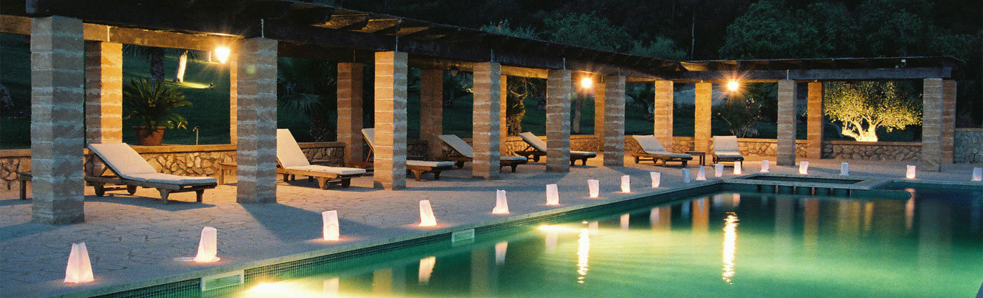 The Son Terrassa pool lit at night, the pergola columns glowing and rows of floating candle-lanterns reflected in the still water